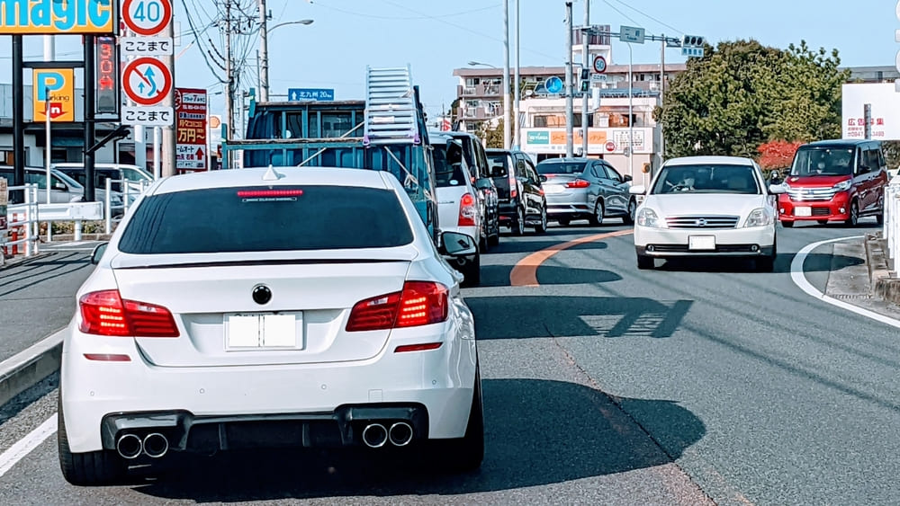 主要幹線道路に出るまでの路地での朝の渋滞｜1車線の道を車が連なり動きそうにないイメージ