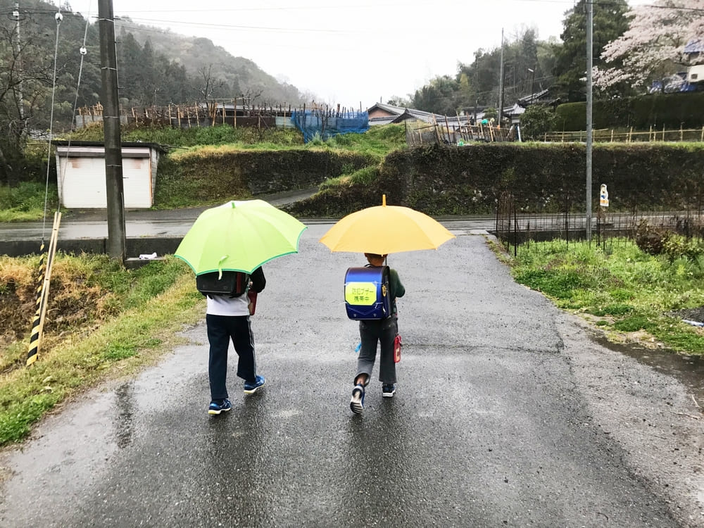 雨の中小学生の低学年児童が道一杯に拡がり通学しているイメージ